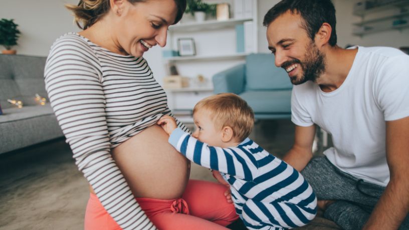 A toddler kisses his mum’s pregnant tummy.