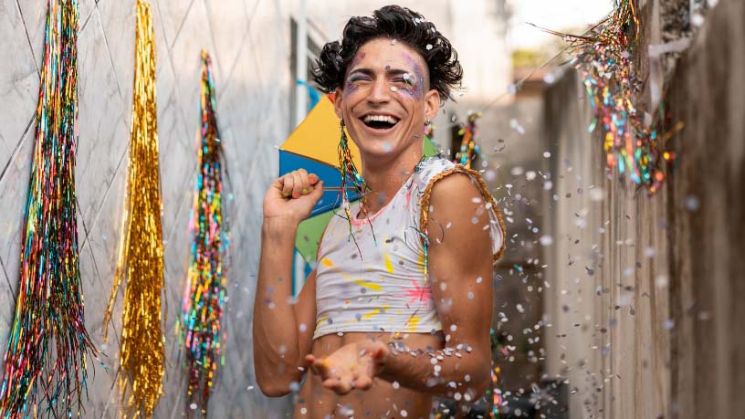 A person with colourful face paint dances in confetti.