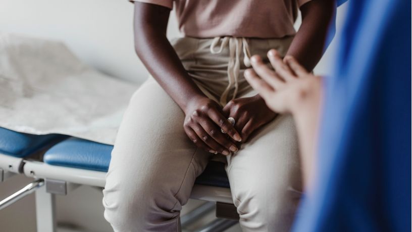 Torso of a woman sitting on a medical bed talking to a nurse.