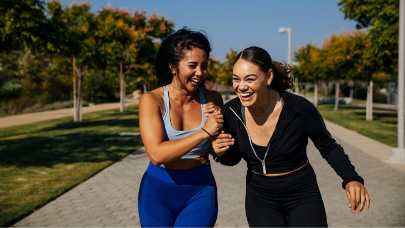 Young female friends laughing together whilst walking in a park