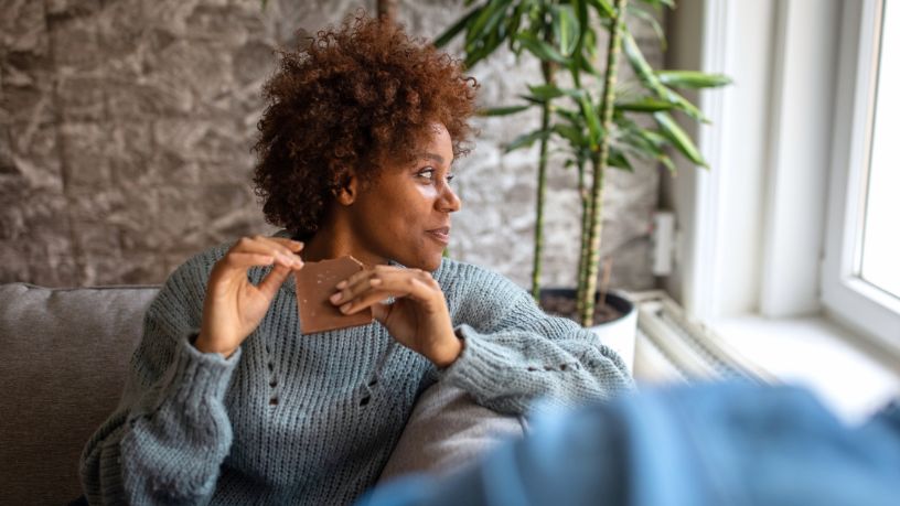 A woman looks out of a window while eating a piece of a block of chocolate.