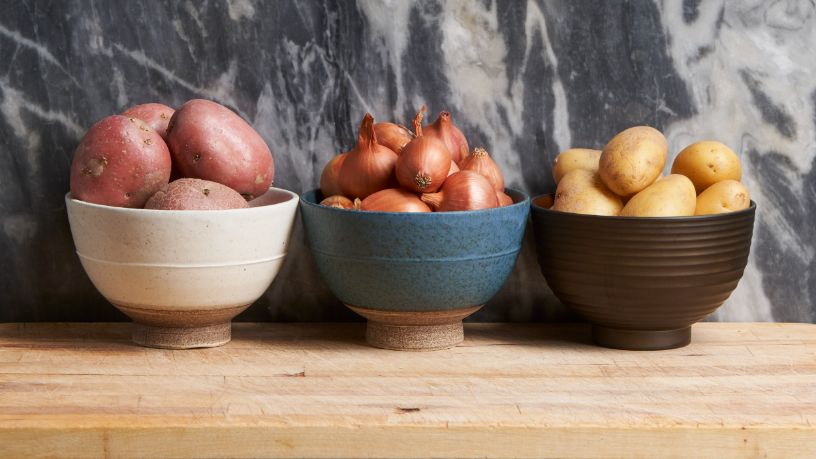 Three bowls on a bench. Two contain potatoes, one contains onions.