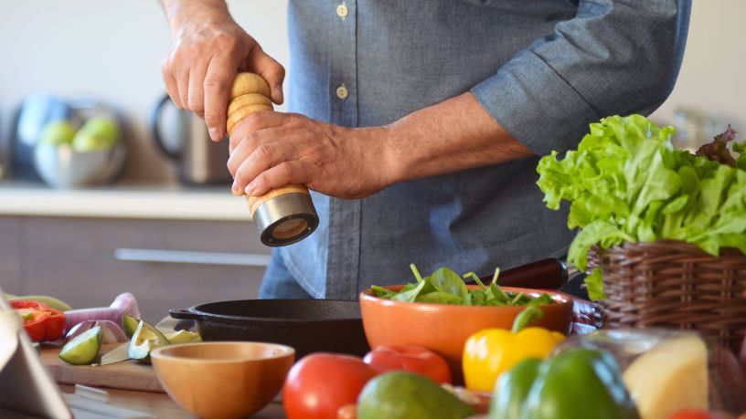 A person grinds salt into a bowl which sits on a bench surrounded by veggies.