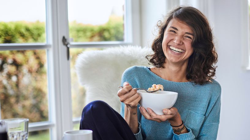 A woman laughs as she eats a bowl of cereal.