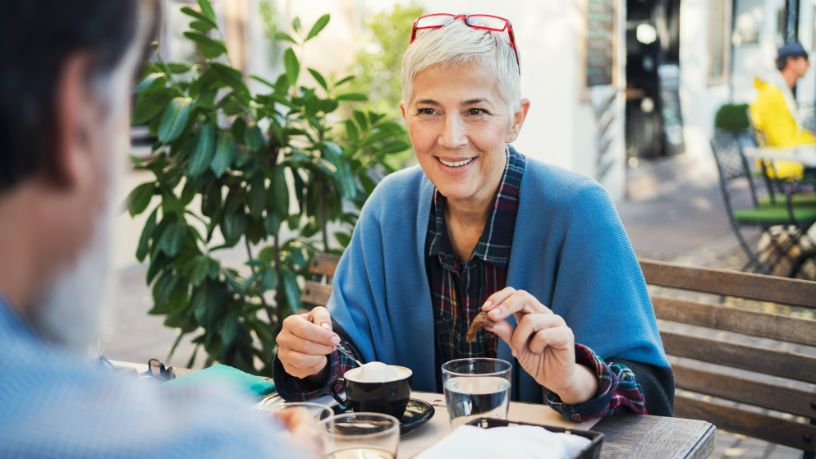 A woman enjoys a cup of coffee with a friend at an outdoor cafe.