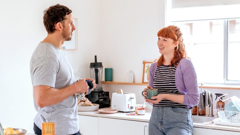 A man and woman speak in a kitchen.
