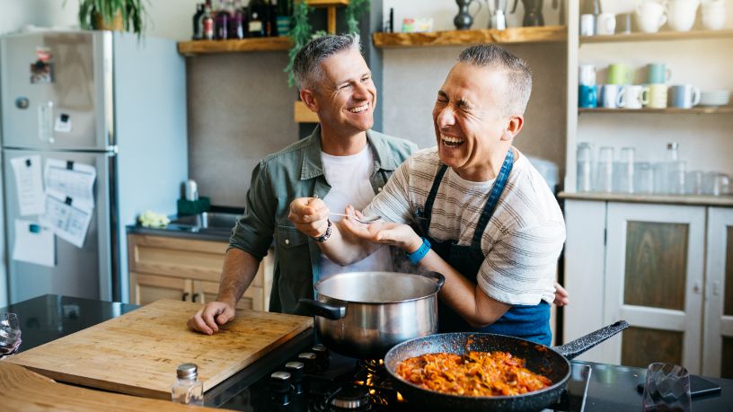 Two men cook together and laugh.