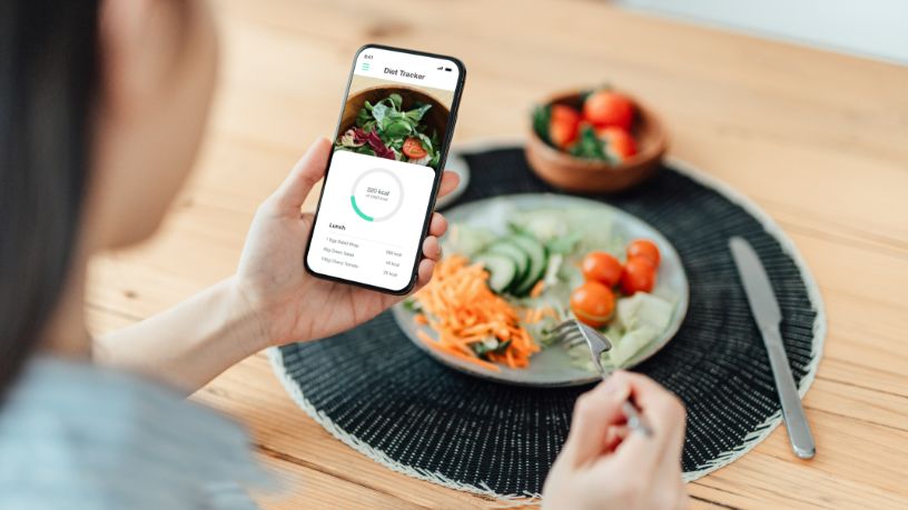 A woman eating a meal looks at nutrition information on her phone.