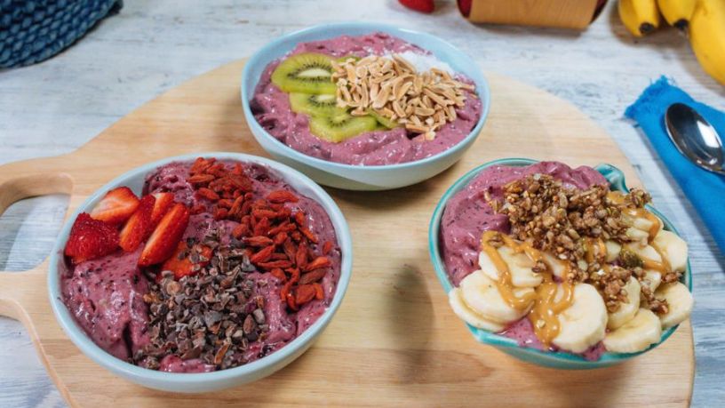 Three thick and creamy smoothy bowls lay on a serving board.