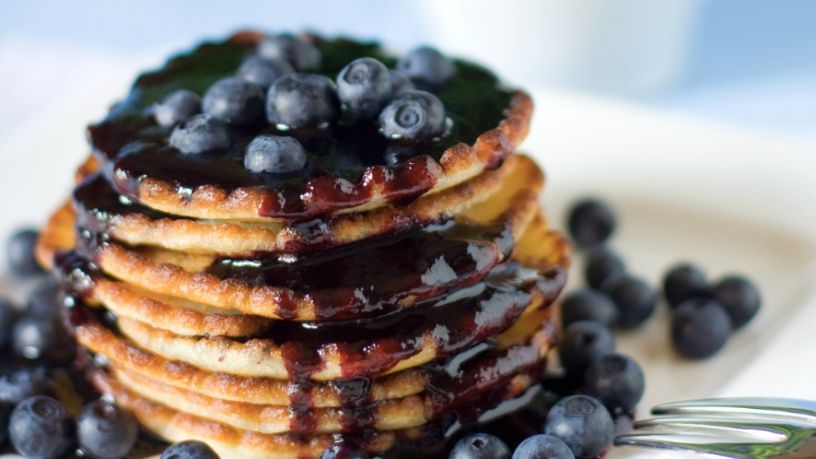 A stack of pancakes is topped with blueberry compote and fresh blueberries.