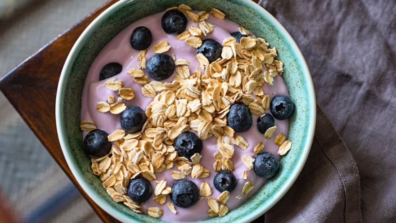 Green bowl of purple yoghurt topped with blueberries and oats