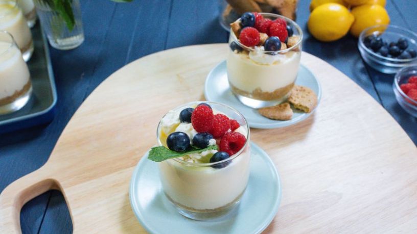Two glasses filled with a biscuit base and cheesecake filling topped with berries