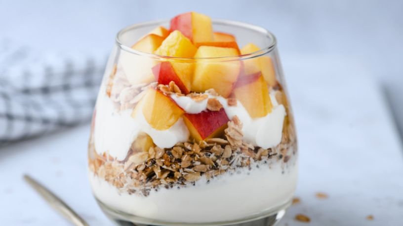 Glass filled with layers of whipped milk, nuts and orange coloured fruit