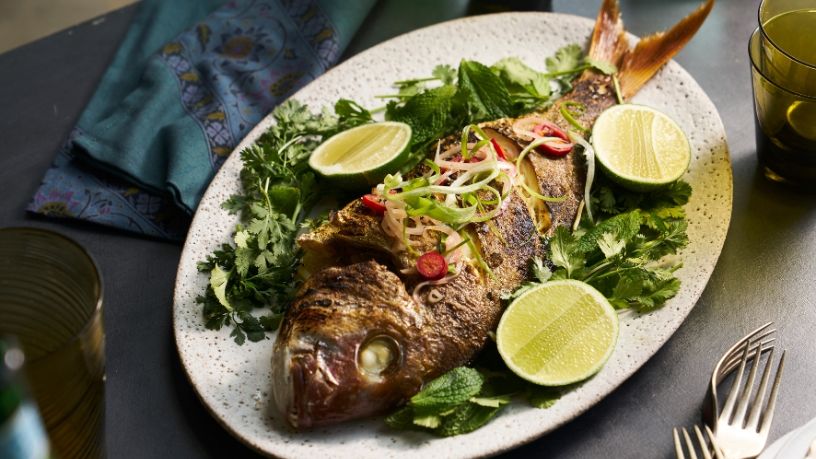 A crispy Asian-style cooked snapper lays on a serving platter with garnishments.