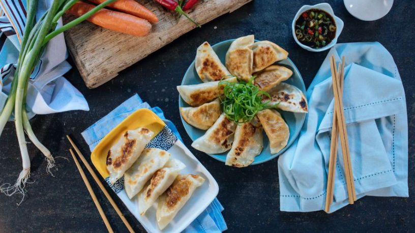 A plate of potstickers sits on a table with various garnishments and dips.