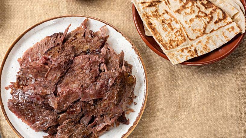 A plate of slow-cooked lamb and a plate of pita bread sit on a dining table.