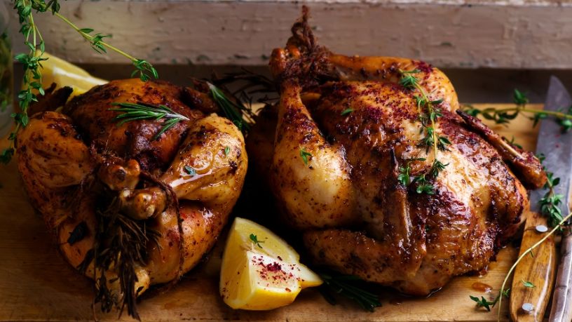 Two roast chickens lay side by side on a chopping board.