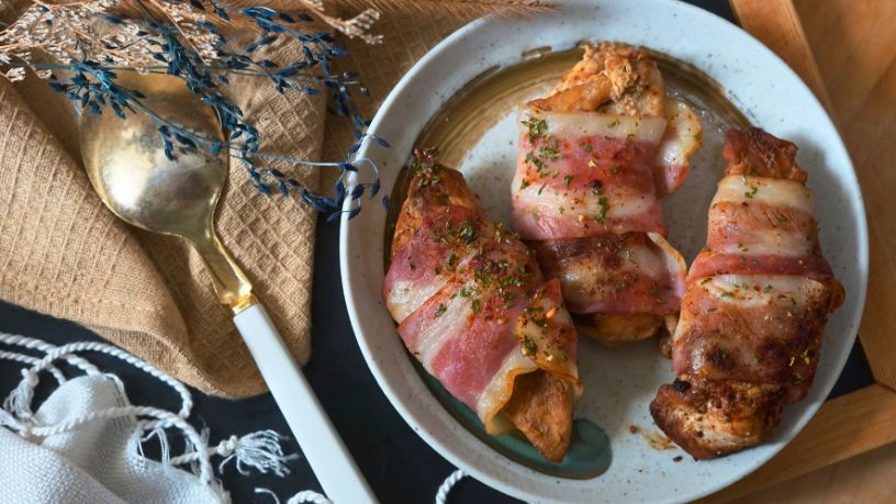 A plate of rolled turkey with prosciutto lays on a rustic dining table.