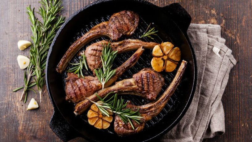 A chargrill pan filled with cooked lamb and various garnishments sits on a table.