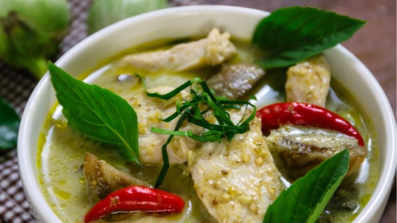 A bowl of Thai green curry sits on a table