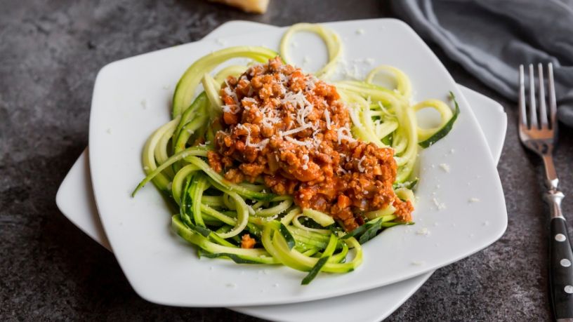 A plate of spaghetti bolognaise on zucchini noodles sits on a dining table.