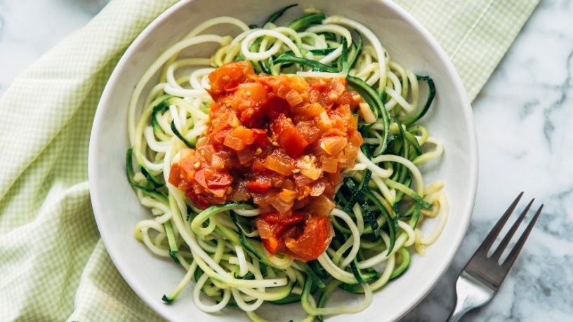 A bowl of zucchini noodles is topped with puttanesca sauce.