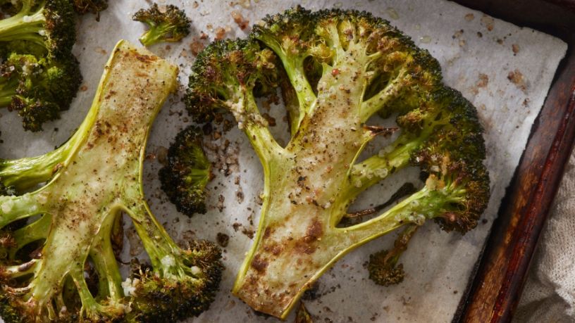 Halves of chargrilled broccoli lay on a baking tray.