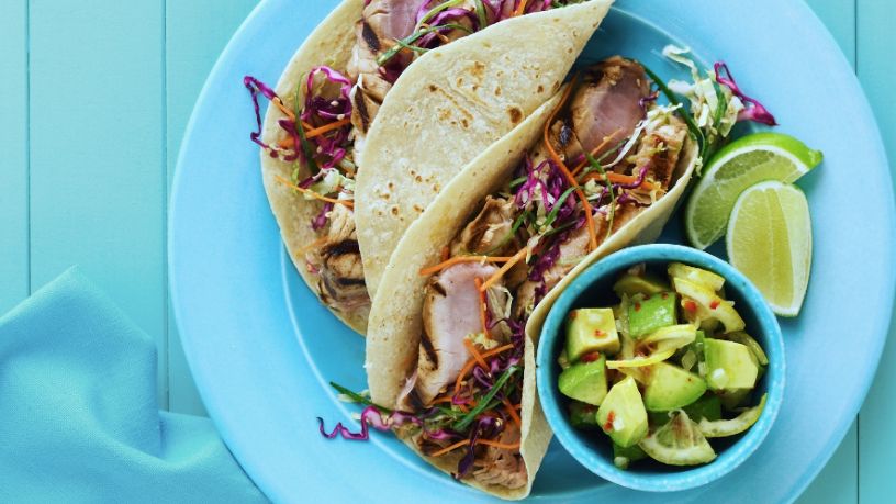 Charred fish tacos with tomatillo salsa verde sit on a blue plate.