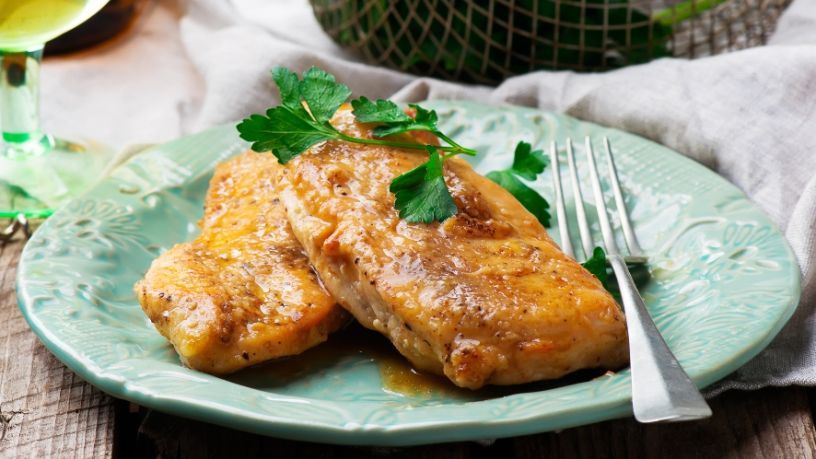 A plate of lemon and rosemary chicken is laid out on a dining table.
