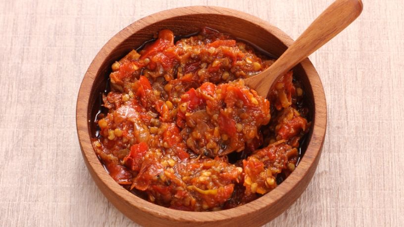 Red tomato and onion mixture in a wooden bowl with a wooden spoon.