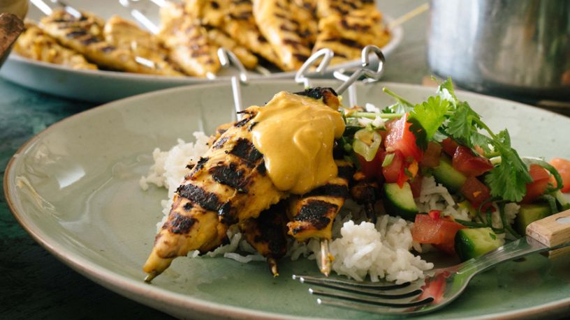 A plate of grilled chicken fillets on a bed of rice with a tomato and cucumber salad.