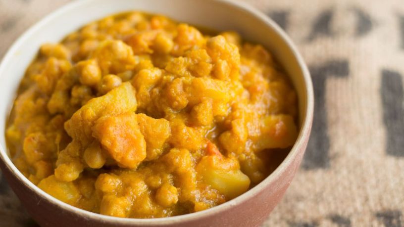 A bowl of yellow dahl filled with chunks of lentils and vegetables.