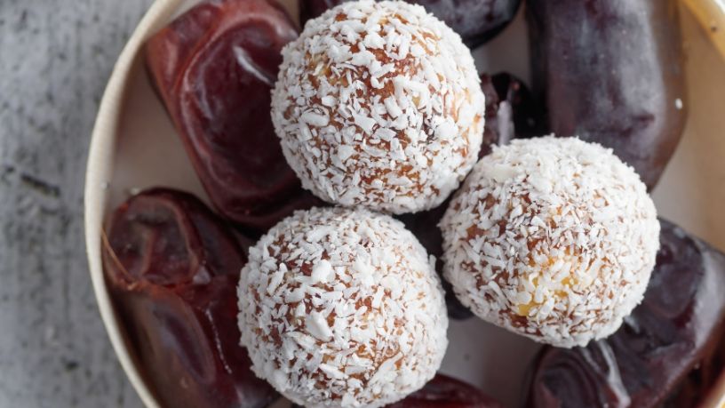 Three coconut and date dream balls are arranged on top of a bowl of dates.