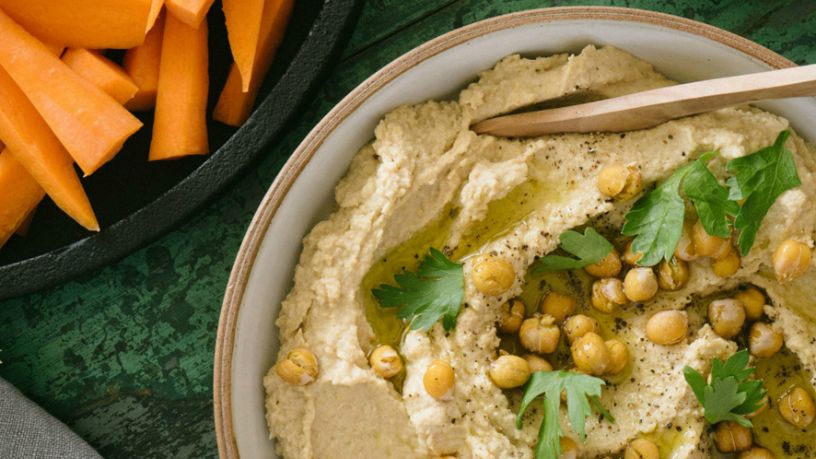 A serving bowl filled with hummus sits next to a bowl of chopped carrots.