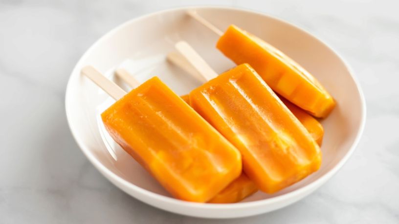 Five mango, pineapple and passionfruit icy poles sit in a bowl.
