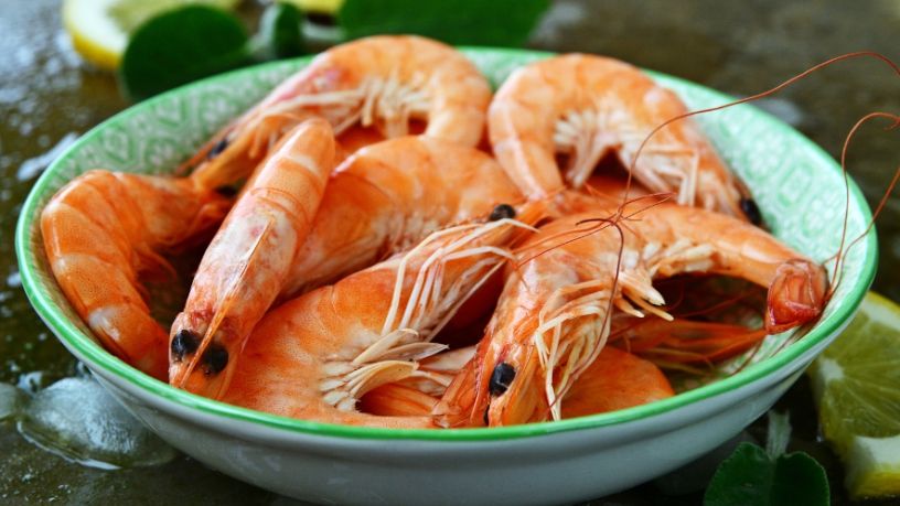A bowl of cooked prawns sits on a table surrounded by lemon slices.