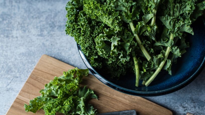 Fresh kale is variously placed in a bowl and on top of an adjoining chopping board.