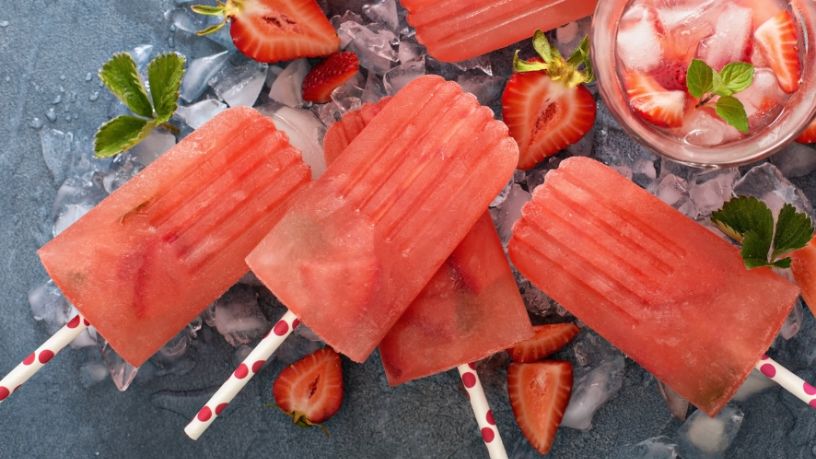 Five watermelon, berry and mint icy poles are playfully arranged with ice and fruit.