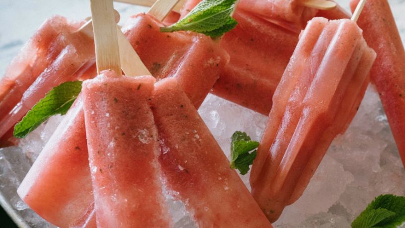 Several watermelon, coconut and mint icy poles lay on ice.