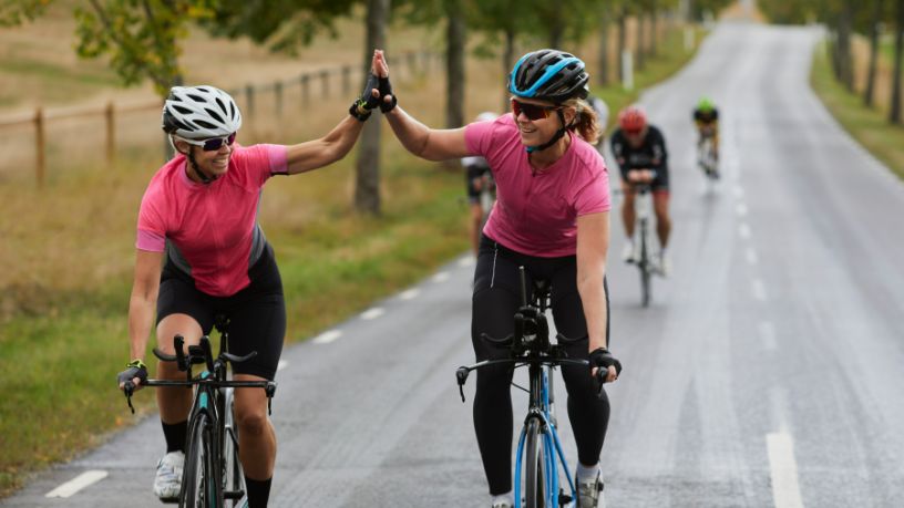 Two women high-five as they ride their bikes.