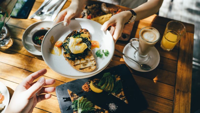 Kitchen staff handing a plate with eggs and spinach on toast to a waiter.