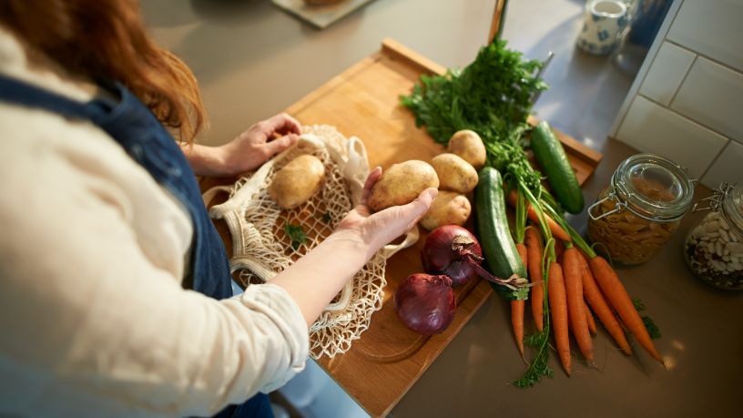 A woman unloads vegetables from a shopping bag.