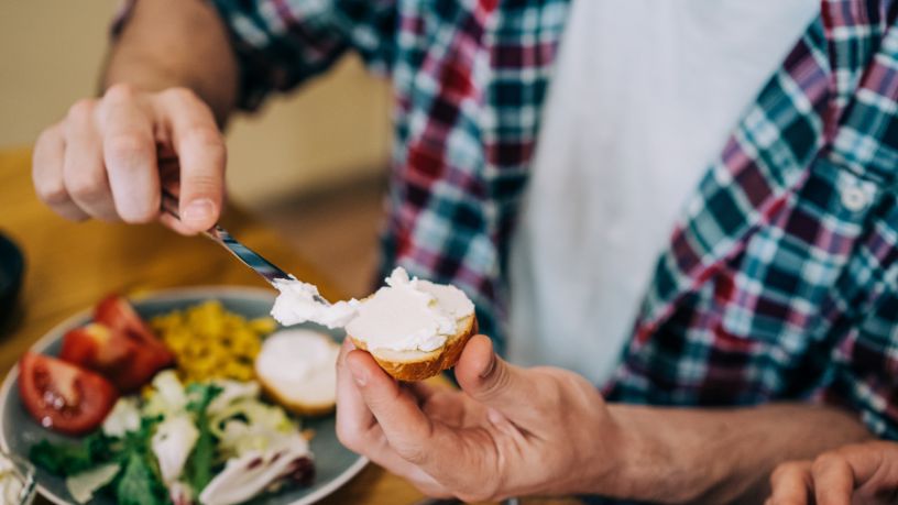 A person with a knife smearing spread onto bread in front of a healthy meal.