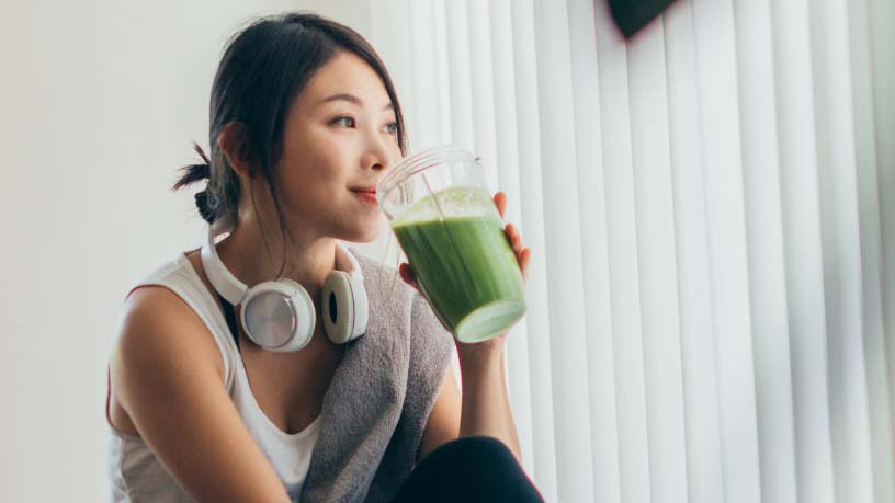 A woman sits on the floor drinking a green smoothie.