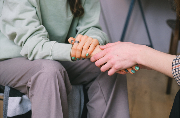 Close up of two people sitting opposite each other holding hands with their faces out of focus