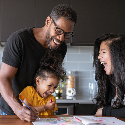 Man and young girl in the kitchen laughing as they draw in a colouring book.