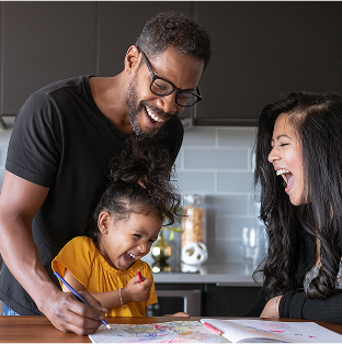 Man and young girl in the kitchen laughing as they draw in a colouring book.